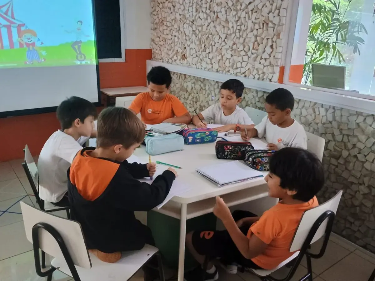 Turma do Fundamental Anos Iniciais trabalhando em grupo numa mesa, com a aula projetada na parede